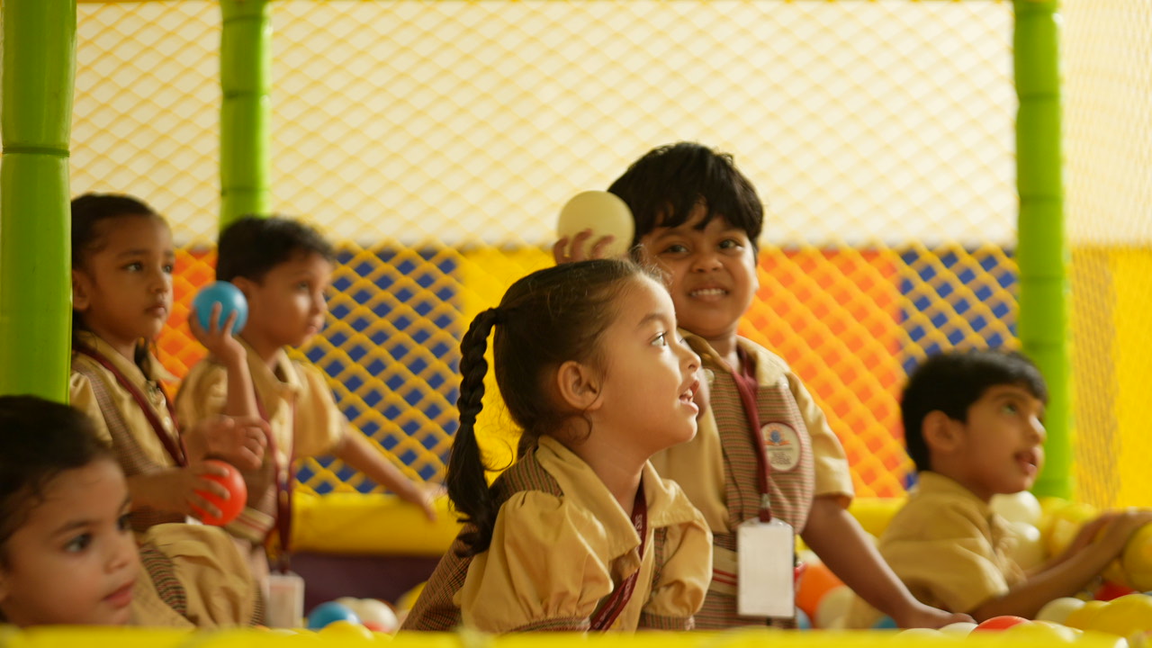 Children laughing and playing with colourful balls in the ball pit at SKS World School