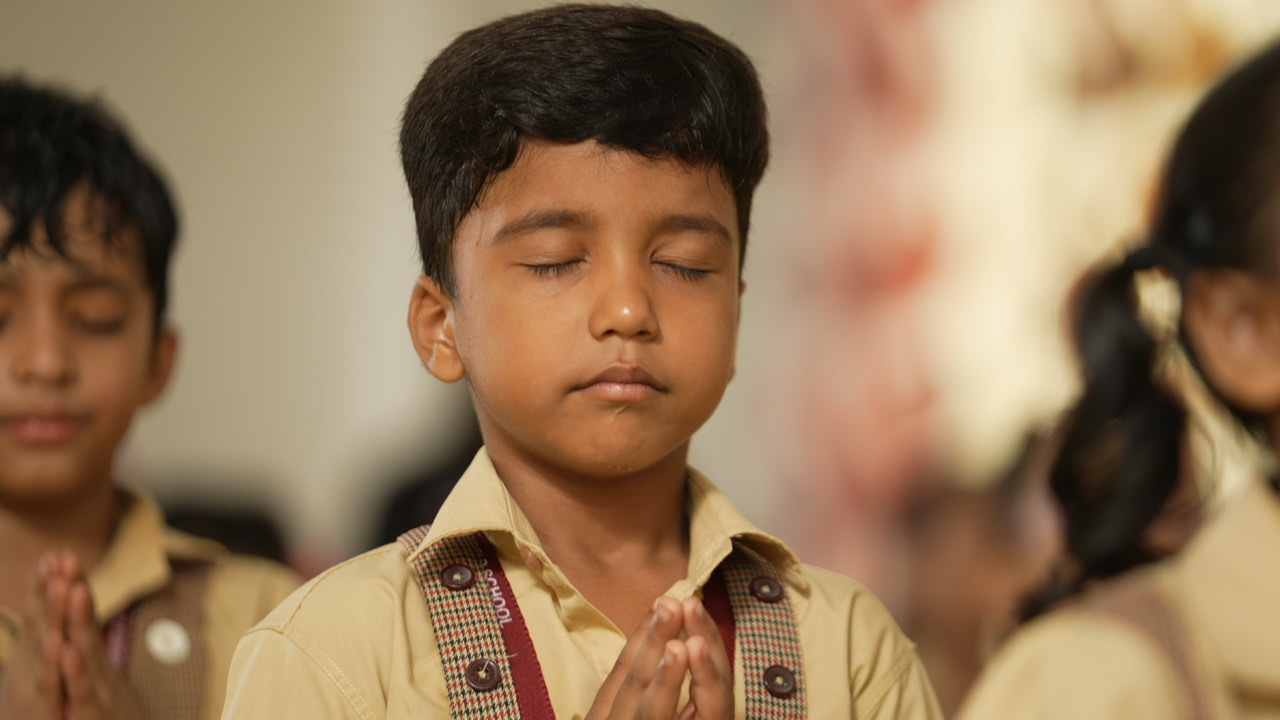 A student with folded hands and closed eyes in prayer at SKS World School